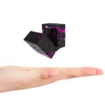 A black magnetic cube with pink splatter design floating above an outstretched hand, demonstrating its compact size and interactive nature.