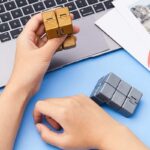 Two small, metallic-colored puzzle cubes placed on a blue surface near a laptop keyboard, perfect for stress relief and cognitive exercises.