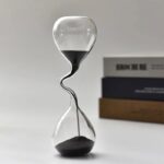 A close-up of a modern hourglass timer with black sand, showcasing its elegant design and precise function for measuring time intervals.