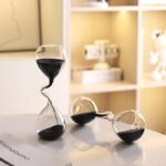 Modern glass hourglass sand timer with black sand, perfect for science-themed decor and educational settings. Stylish and functional, ideal for classrooms or home science displays.