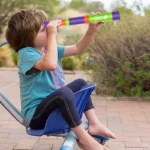 Child girl using a colorful telescope outdoors.