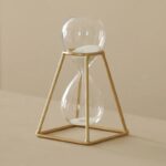 Sand timer with a clear glass bulb and white sand, encased in a gold geometric frame, ideal for science decor and educational purposes.