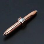 Close-up of a sleek rose gold ballpoint pen with silver accents on a dark background, showcasing its modern design and polished finish.