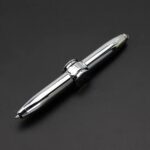 A shiny metallic ballpoint pen with a smooth finish, lying on a dark background, showcasing its modern design and reflective surface.