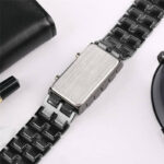 Close-up of a vintage metal wristwatch with a rectangular face and black strap, showcasing its sleek design and brushed metal finish.