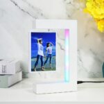 Modern digital photo frame displaying a beach scene with two women walking on the shore, set against a white marble background with yellow flowers.