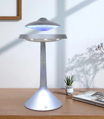 Modern UFO-shaped LED lamp with blue light on a wooden desk, accompanied by a potted plant and a magazine, creating a sleek and futuristic decor element.