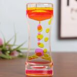 Colorful liquid motion timer with yellow, pink, and orange droplets inside a transparent hourglass-shaped container.