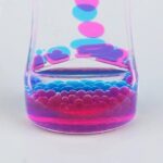 Vibrant pink and blue liquid with floating bubbles and droplets in a clear glass container, demonstrating a fun and educational science experiment.
