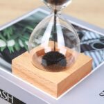 Sand timer with black sand flowing inside a glass bulb mounted on a wooden base, used for educational and decorative purposes.