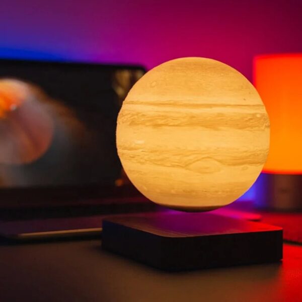 A spherical moon lamp emitting warm light, placed on a black stand with colorful ambient lighting in the background, creating a cozy and modern decor setting.
