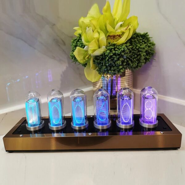 Modern violet Nixie tube clock displaying time, placed on a sleek black and gold stand with a decorative flower arrangement in the background.