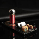 Small Tesla coil demonstration with copper coils, transformer, and metallic sphere on a black background.