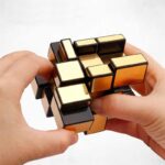 Hand holding a magnetic puzzle cube with black and gold-colored pieces, demonstrating a challenging brain teaser toy for cognitive development and problem-solving skills.