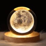 Illuminated moon globe lamp resting on a wooden base, showcasing detailed lunar surface features in a dark setting.