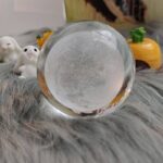 A clear glass crystal ball resting on a plush gray surface, with tiny bubbles inside, surrounded by cute bunny and pumpkin decorations, perfect for science decor or educational displays.