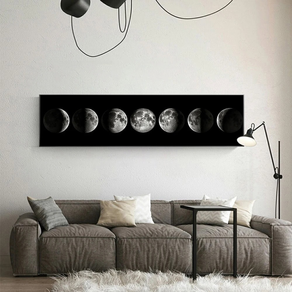 A sleek black wall art piece displaying the different phases of the moon, mounted above a contemporary gray sofa in a minimalist living room.