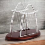 Elegant metallic Newton's Cradle on wooden base, demonstrating conservation of momentum and energy, ideal for science decor and educational purposes.