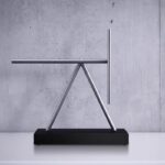 Sleek metallic sculpture with geometric design, displayed on a black base, ideal for science-themed decor and educational spaces.