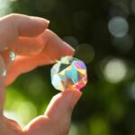 Prism crystal held between fingers reflecting rainbow colors.