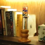 Vintage scientific glass tube with colorful liquids and bubbles, placed on a wooden stand, surrounded by books and decorative items in a cozy study setting.