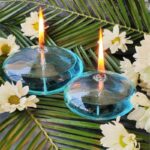 Elegant blue glass floating candle holders with lit tea lights, surrounded by tropical leaves and white flowers, creating a serene and decorative ambiance.