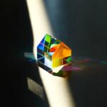 A vibrant, multi-colored glass prism casting rainbow reflections on a dark surface, demonstrating light refraction and dispersion.