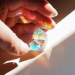 Hand holding a colorful diamond-shaped prism that refracts light into vibrant rainbow colors, creating a captivating visual effect.