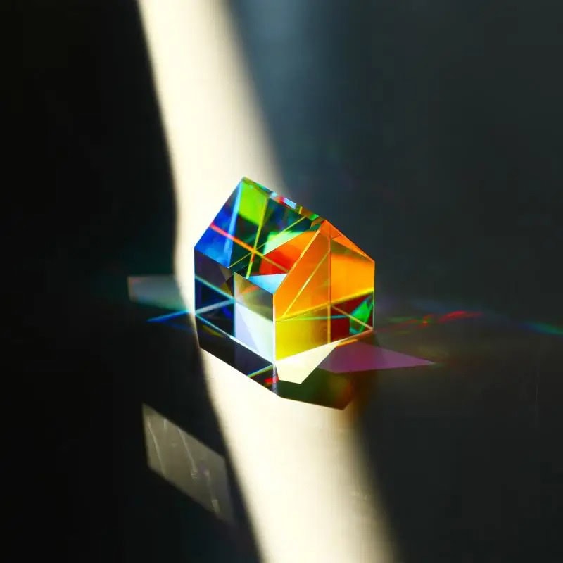 A vibrant, multi-colored glass prism casting rainbow reflections on a dark surface, demonstrating light refraction and dispersion.