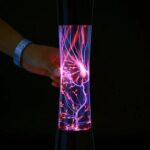 Hand holding a plasma ball emitting colorful lightning-like electrical discharges in a dark environment.