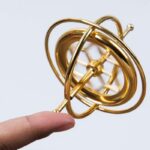 Close-up of a gold-colored atomic model held by a person's finger, used for science education and home decor.