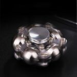 Close-up of a metallic fidget spinner in motion, showcasing its spinning blades and shiny surface against a dark background.