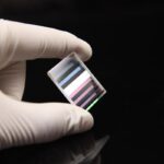 High-tech optical filter held by a gloved hand against a black background.