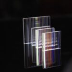 Acrylic optical illusion art pieces with colorful light reflections on a black background.