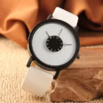 Stylish minimalist wristwatch featuring a distinctive dial with a small black sub-dial displaying hours and minutes, set against a white face with a black case and white strap.