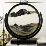 Decorative mountain landscape sand art in a circular frame, showcasing layered black, white, and gold sands creating a scenic mountain view.