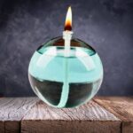 Glass oil lamp with a floating wick and flame, set on a wooden surface against a dark background.