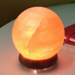 A spherical moon-shaped night light emitting a warm, orange glow, resting on a wooden base. Perfect for adding a cozy, celestial ambiance to any room.