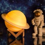 Decorative Saturn planet lamp with wooden stand and astronaut figurine, perfect for science-themed decor and educational spaces.