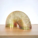 A metallic spiral sculpture made of interconnected gold-colored rings, forming a smooth, curved shape placed on a wooden surface.