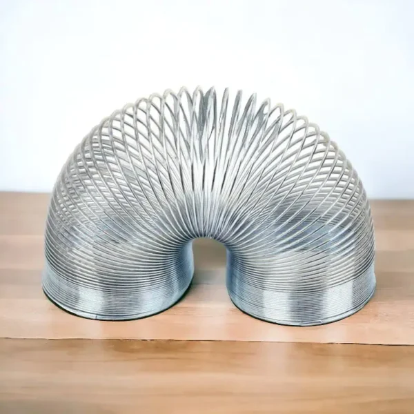 A metallic coil sculpture shaped like a flexible, curved tube, showcasing intricate spirals and a shiny surface, placed on a wooden surface.