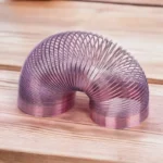 A shiny metallic spiral sculpture with a smooth, reflective surface, shaped like a coiled tube, placed on a wooden surface. Perfect for science-themed decor and educational displays.