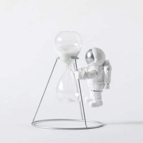 Astronaut figure holding a large hourglass with white sand, standing on a minimalist metal stand.