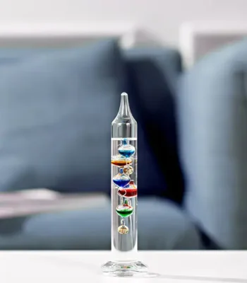 A colorful lava lamp with multiple layers of vibrant liquids and floating objects, placed on a white surface with a blurred sofa in the background.