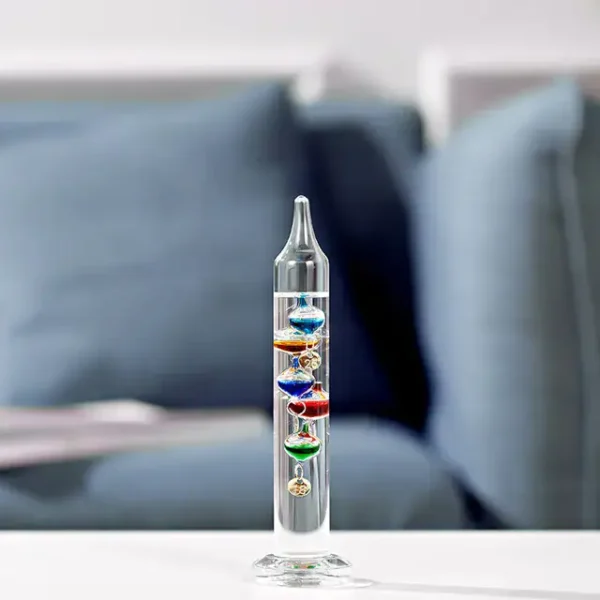 A colorful lava lamp with multiple layers of vibrant liquids and floating objects, placed on a white surface with a blurred sofa in the background.