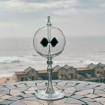 Glass wave energy demonstration device with black square paddles, on a patterned surface overlooking the beach.