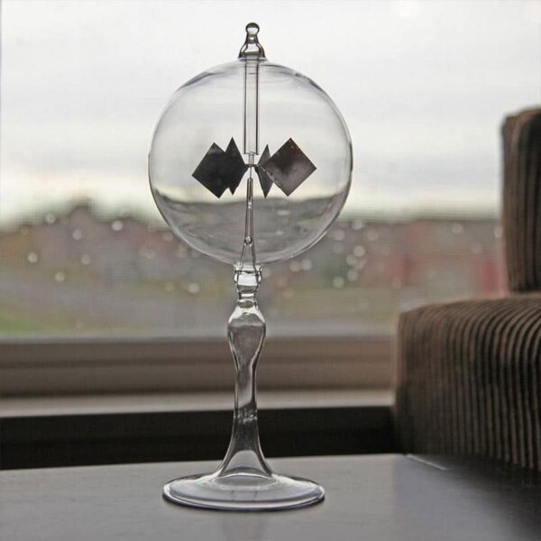 A glass pendulum with magnetic squares inside, demonstrating magnetic forces, placed on a windowsill with a blurred cityscape background.