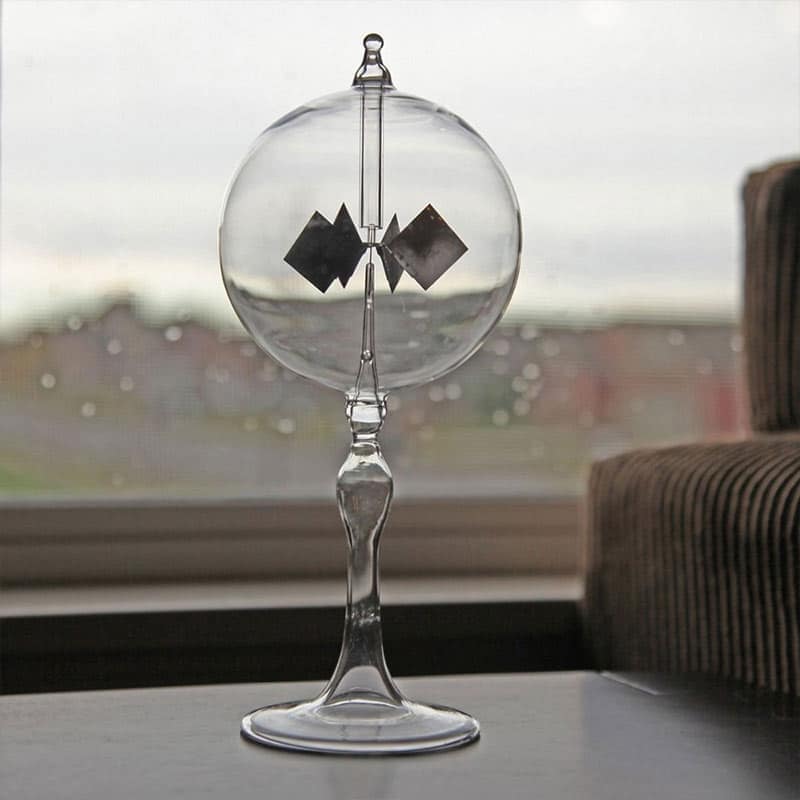 Magnetic Pendulum Experiment A glass pendulum with magnetic squares inside, demonstrating magnetic forces, placed on a windowsill with a blurred cityscape background.
