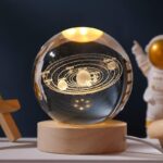 A detailed glass globe showcasing the solar system with planets and their orbits, illuminated with golden accents, mounted on a wooden base.