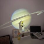 Shadow of Saturn projected on the wall with a plant and laptop on a desk, creating a space-themed decorative setup.